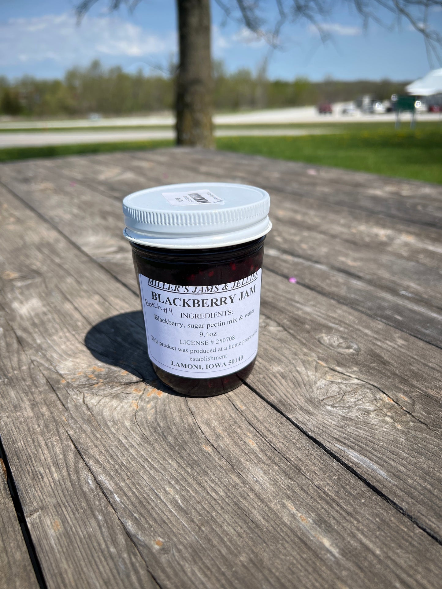 Amish Country Store Miller’s Blackberry Jam jar with blackberries and jam spread on a wooden surface.