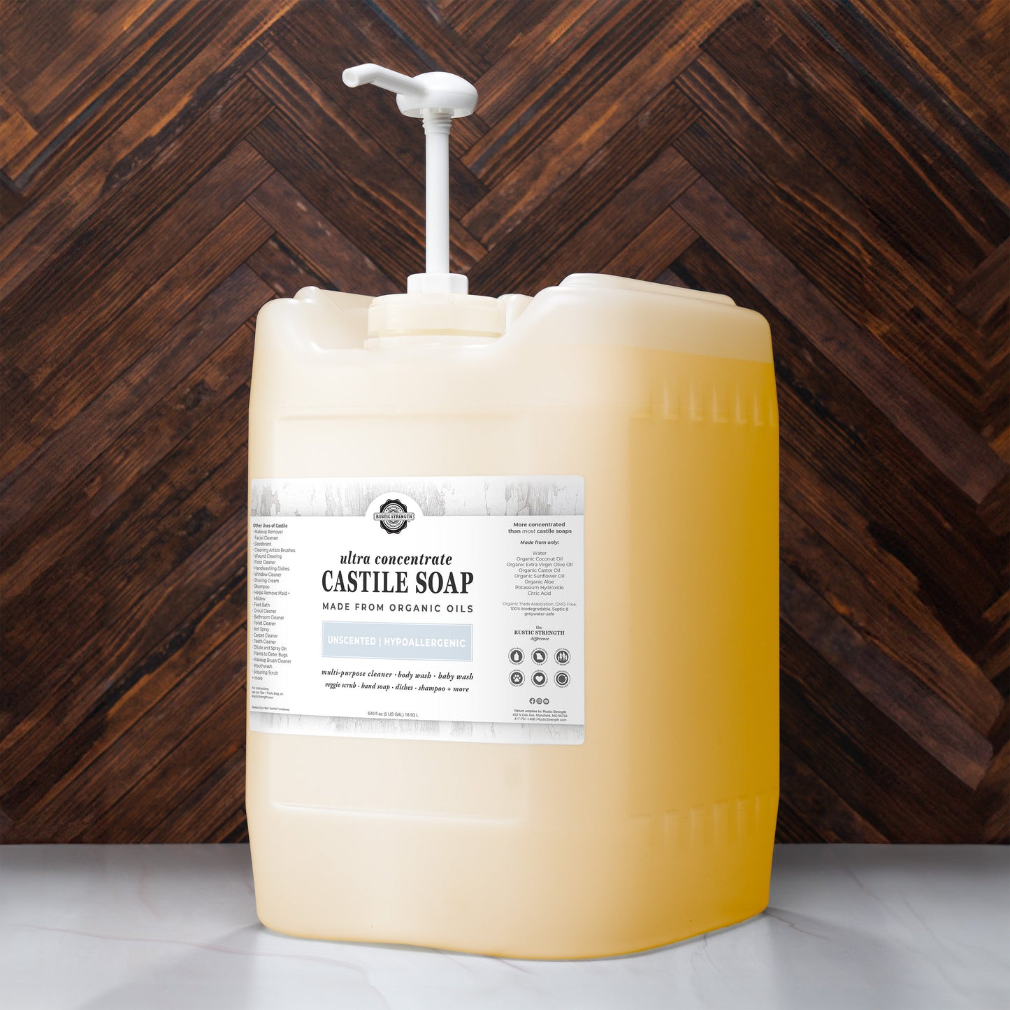 A large pump dispenser of Rustic Strength Castile Soap - Ultra Concentrate | Unscented, made from organic oils and filled with yellow liquid, sits on a countertop in front of a dark herringbone wall, ready for versatile cleaning.