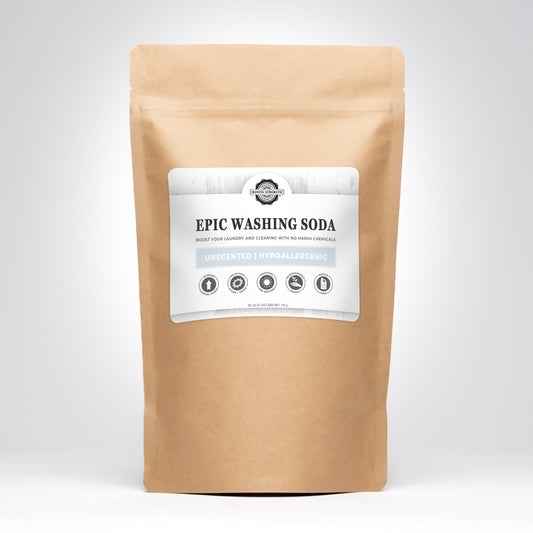 A brown paper bag labeled Epic Washing Soda by Rustic Strength, featuring text promoting its unscented, hypoallergenic Laundry Boost formula, stands upright against a plain light gray background.