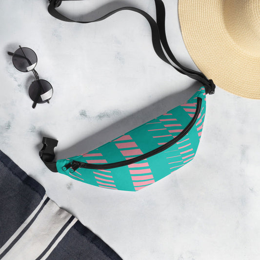 Fabric fanny pack with teal and pink geometric pattern shown on a light gray surface next to sunglasses and a straw hat