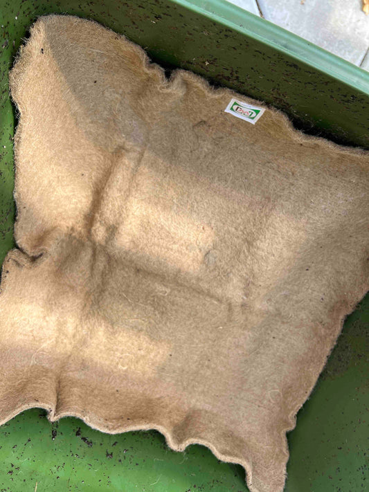 Memes Worm Blanket by Memes Worms is a square, beige felt liner placed inside a green rectangular container with visible soil residue, making it ideal for composting in your worm bin.