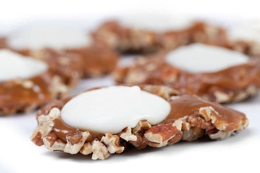 White Chocolate Caramillicans pecan treats by Millican Pecan, individual white chocolate-coated pecan candies on a white background.