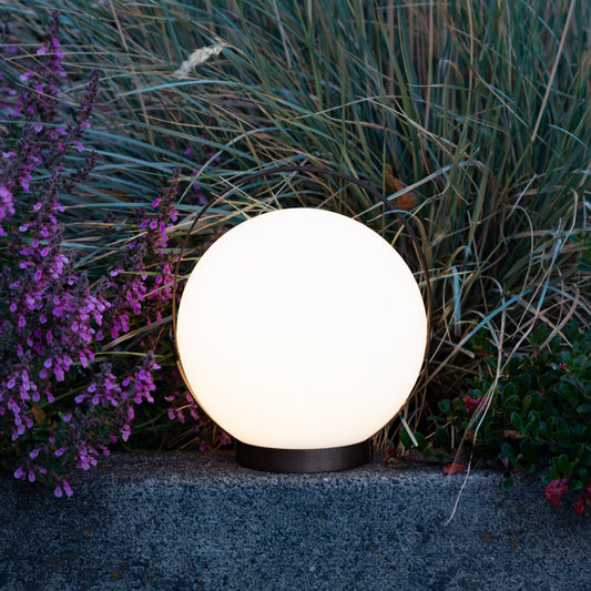 Allsop Home & Garden Moonrise portable rechargeable LED lantern emitting bright light in a dark outdoor setting.