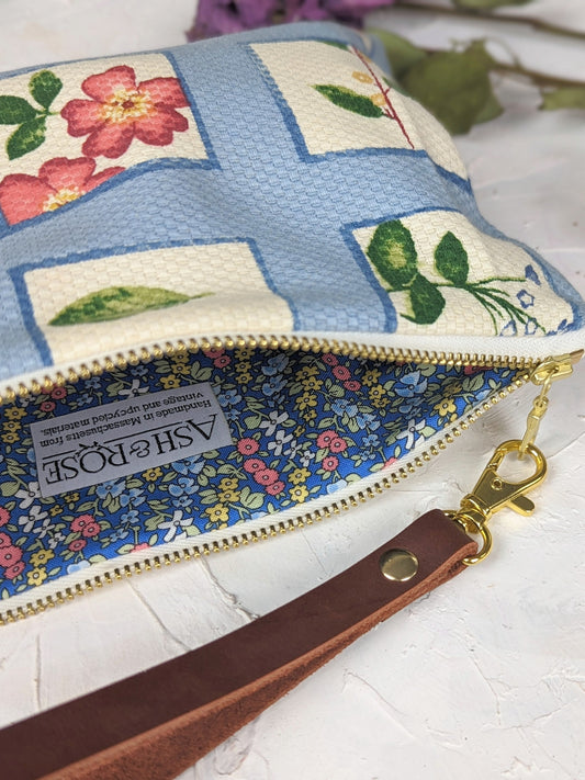 The Summer Meadow Wristlet Purse by Ash & Rose features a blue and white floral pattern, limited edition design, gold zipper, blue floral lining, brown handmade leather wrist strap with gold clasp, and an Ash & Rose label.