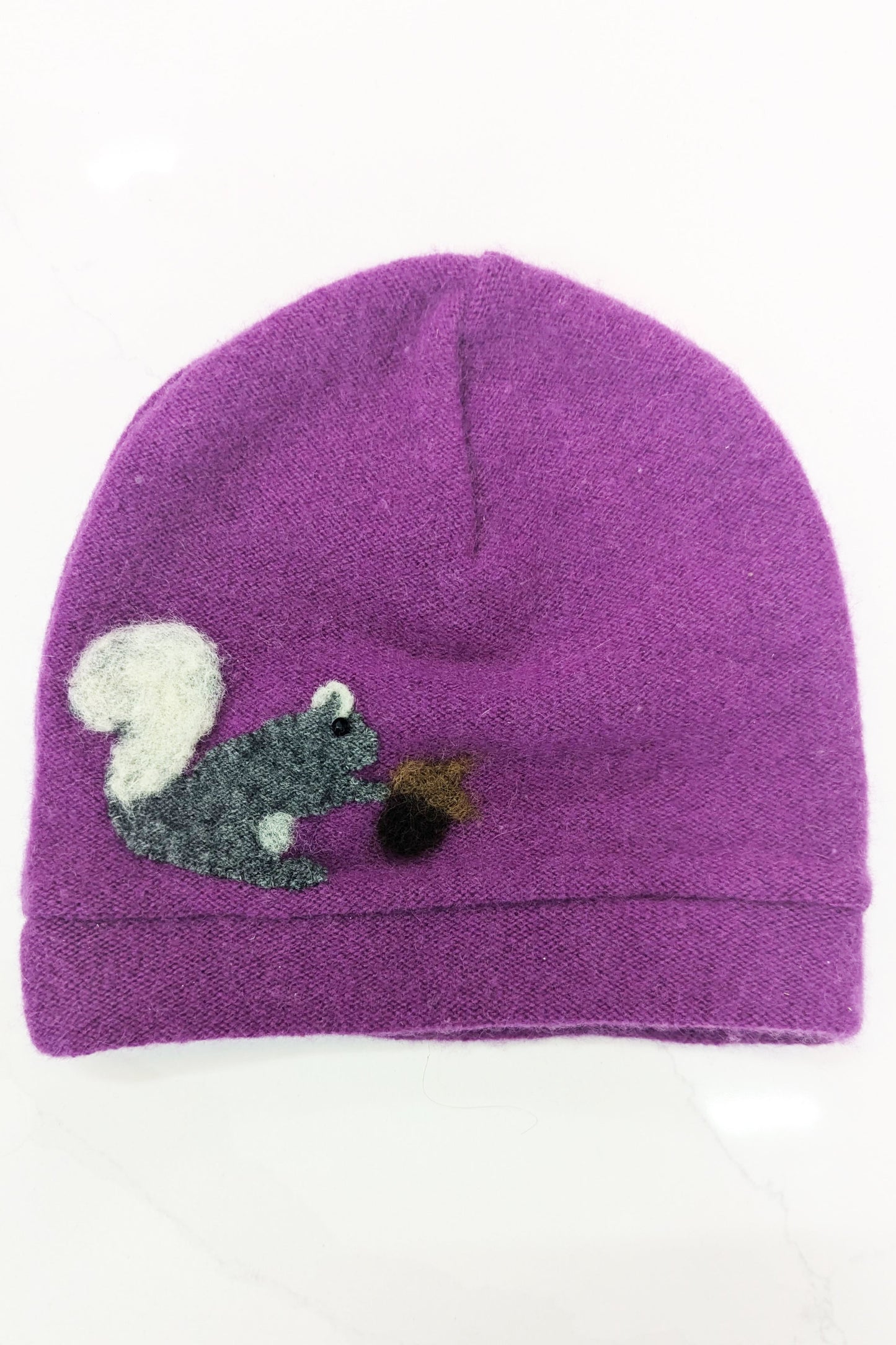 The Ash & Rose Squirrel Cashmere Hat - Toddler is a purple knit beanie featuring a felt applique of a gray squirrel with a white tail holding a brown acorn on the front.