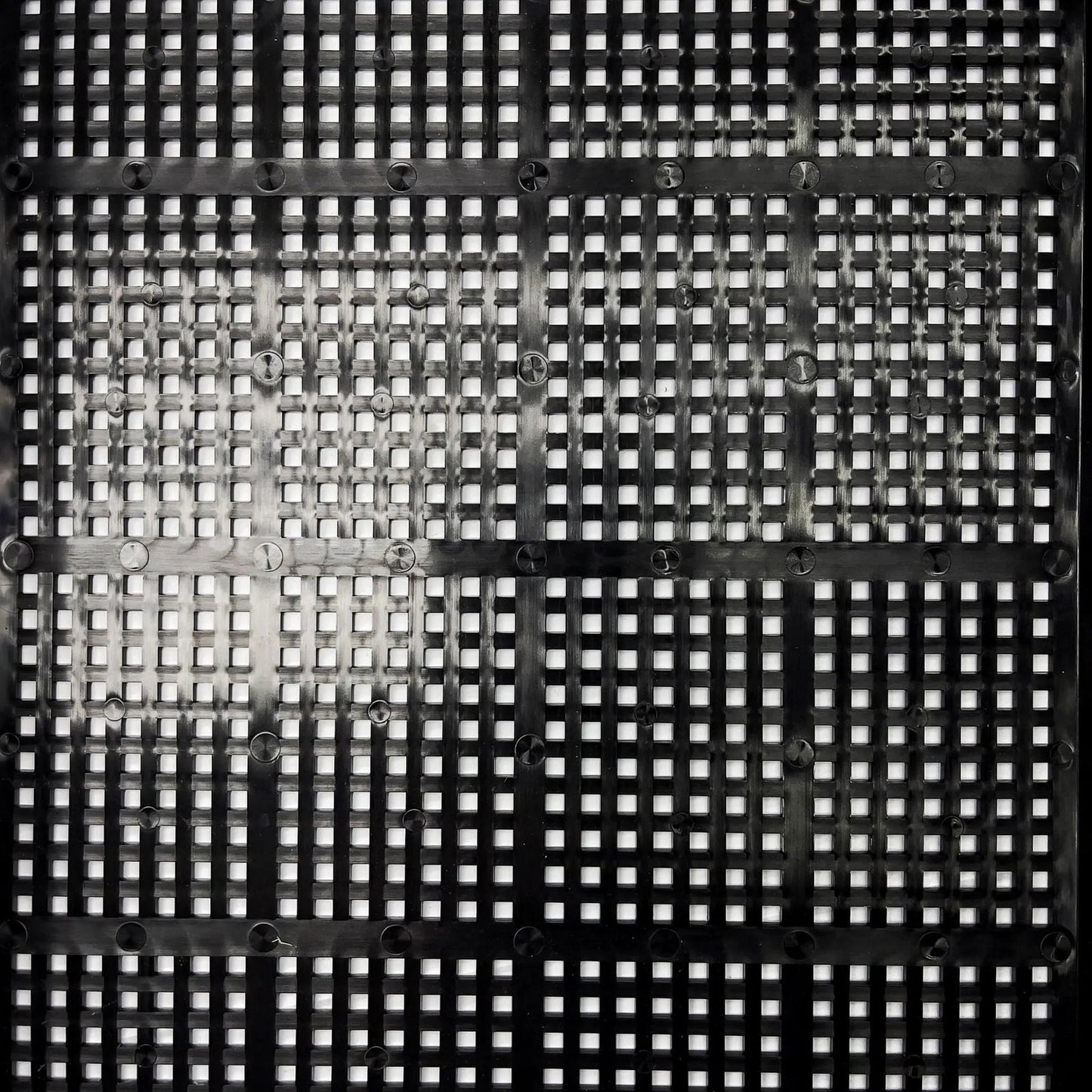 The 1020 Mesh Deep Extra Strength Trays by Bootstrap Farmer feature a geometric black metal mesh pattern with light filtering through the squares, similar to heavy-duty polypropylene trays. Intersecting horizontal and vertical strips are secured with small rounded fasteners.