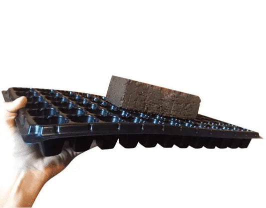 Plastic seedling tray with a textured brown brick resting on top showing multiple small compartments and a dark blue hue.