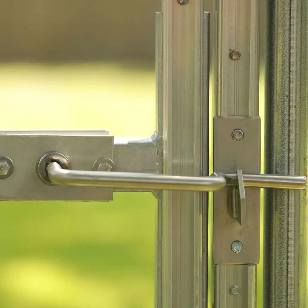 Close-up photograph of a metallic latch and door system showing aluminum framing bolts and a horizontal locking bar against a blurry green background