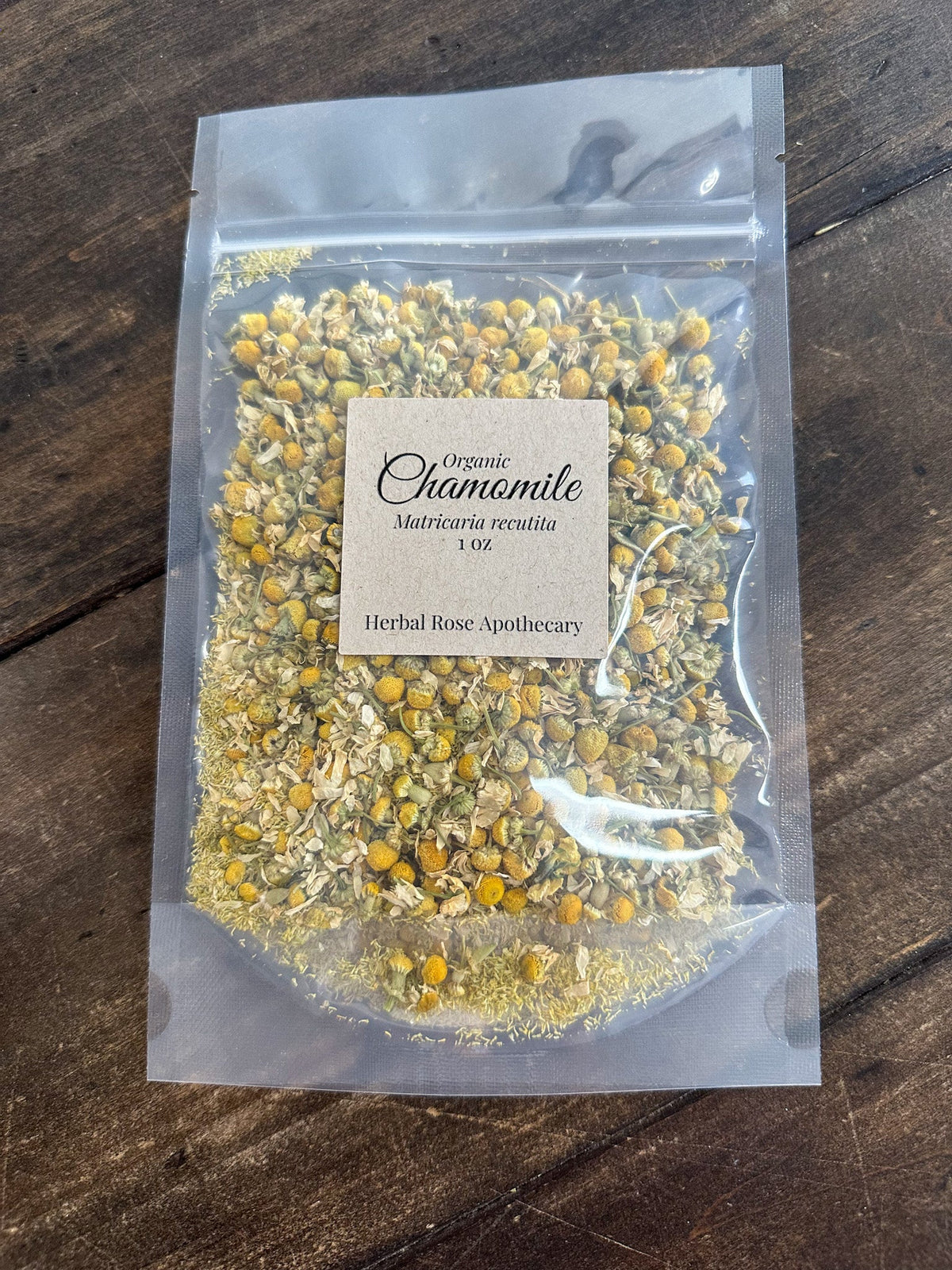Dried organic chamomile herbs in a 1-ounce package from Herbal Rose Apothecary, showing fresh yellow chamomile flowers and stems.