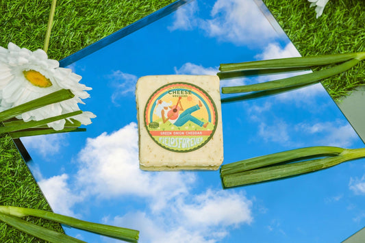 Slices of "Fields Forever" Green Onion Cheddar cheese by Cheese Brothers, Inc., showing vibrant green onions mixed in creamy cheddar.