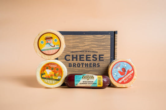 Cheese Brothers Inc. cheese and sausage sampler 4-pack featuring assorted cheeses and cured sausages on a wooden board.