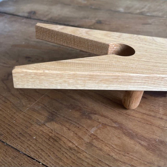 The Celtic Farm’s English Boot Jack - White Oak features a V-shaped notch and circular hole, handcrafted for easy removal of garden boots. Shown resting on wood, this rustic boot puller combines function with classic style.
