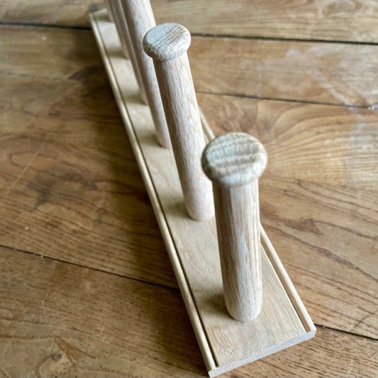 A close-up of The Celtic Farm English Wellington Boot Rack - White Oak 2 Pair, featuring three vertical pegs on a rectangular base, displayed on wood. Perfect for stylishly organizing garden boots.