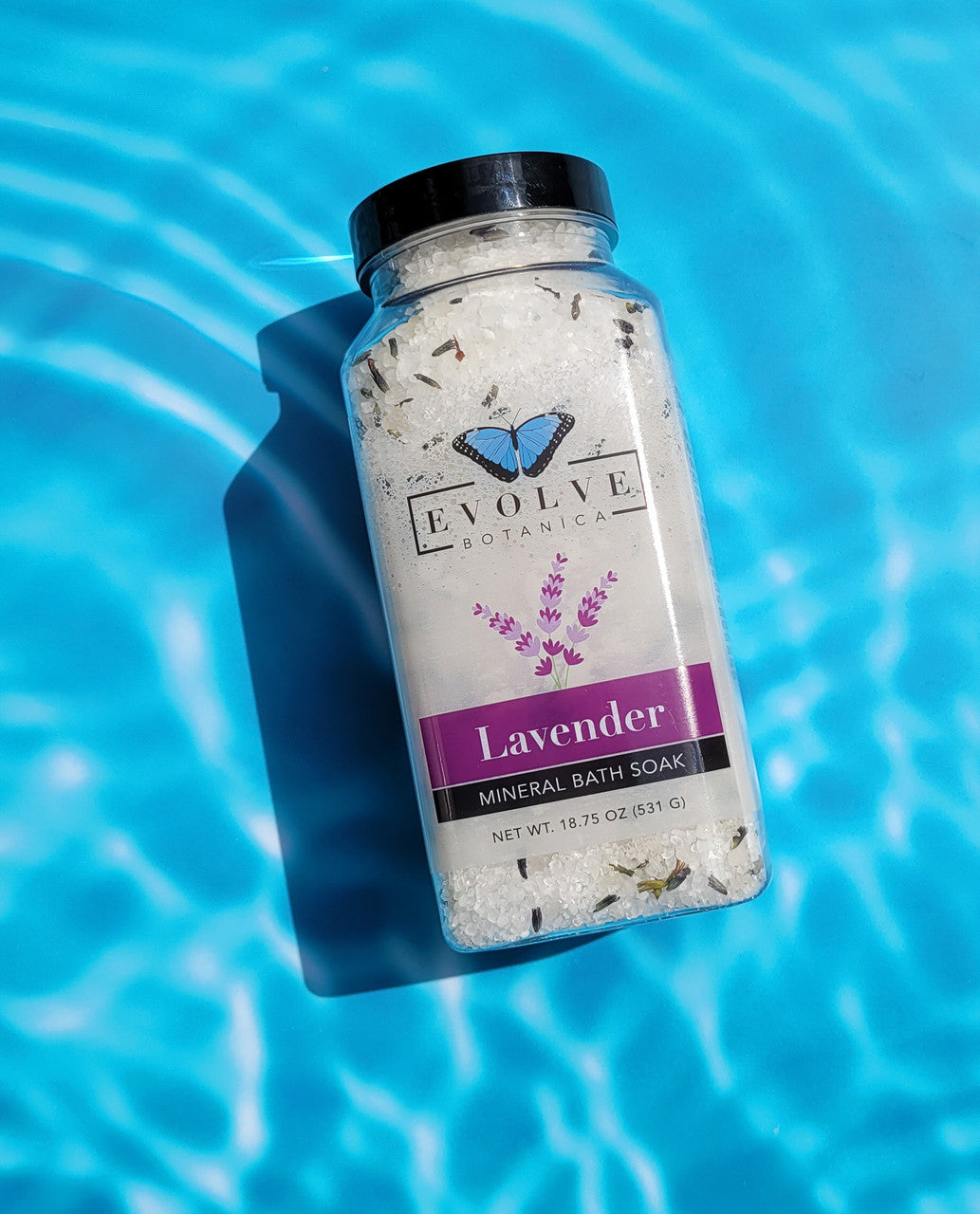 Evolve Botanica Mineral Soak Lavender Spa bath salt in a jar with lavender flowers and a wooden scoop, relaxing spa setting.