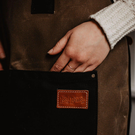 Waxed canvas apron from The Local Branch, USA made, shown with adjustable straps and durable stitching in a fall-themed setting.