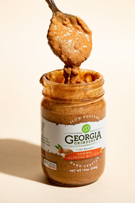 Georgia Grinders 12 oz nut butter assortment including almond, cashew, pecan, and hazelnut butter jars on a wooden surface.