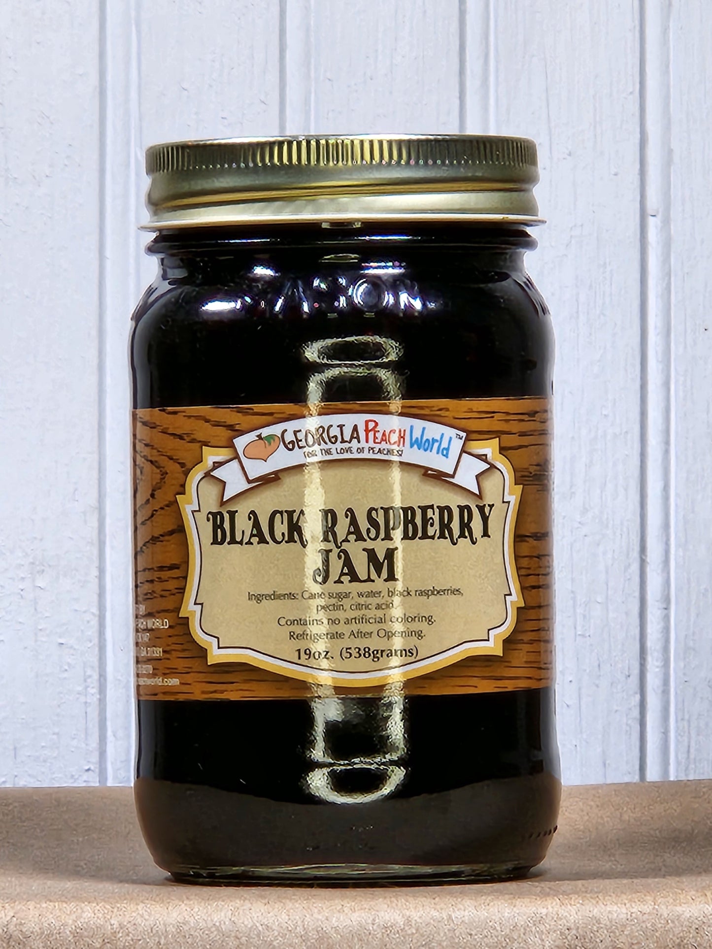 Black raspberry jam by Georgia Peach World in a glass jar with fresh raspberries, showcasing its rich, dark color and fruit texture.