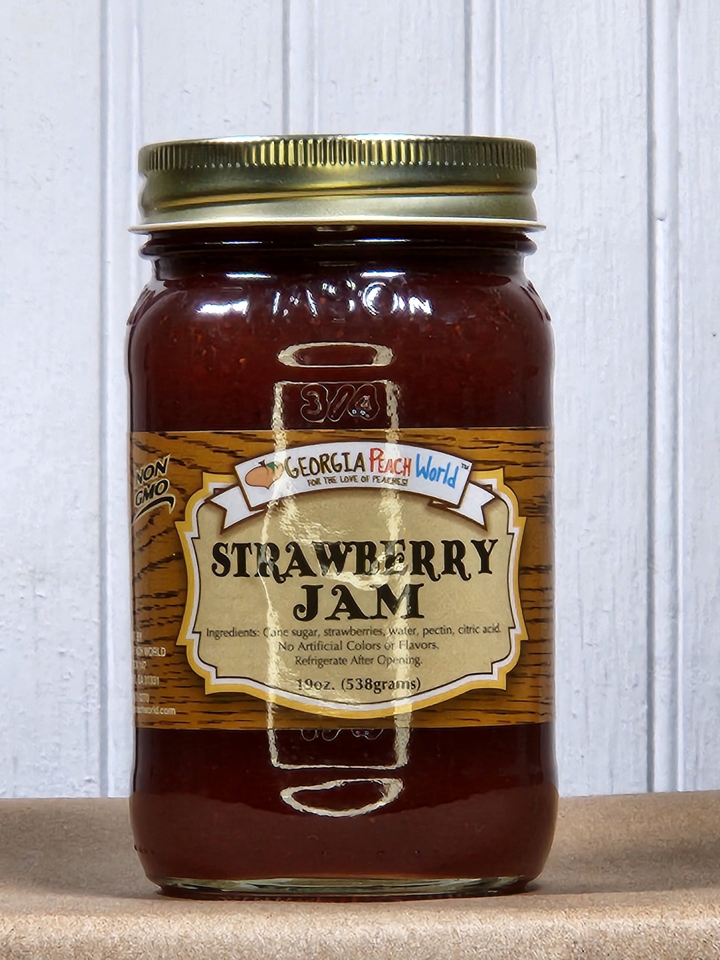 Glass jar of Georgia Peach World strawberry jam with a spoonful showing the bright red, chunky fruit spread.