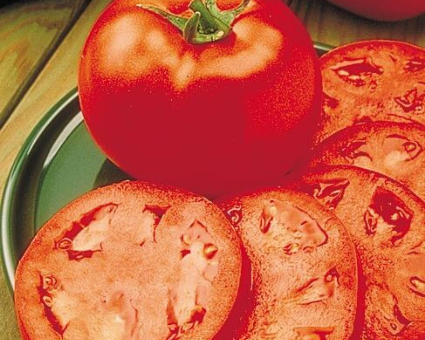 A whole ripe tomato and juicy slices showcasing the red interior are displayed on a green plate atop a wooden surface—grown from Homestead 24 Tomato Seeds by Seeds 'n Such.