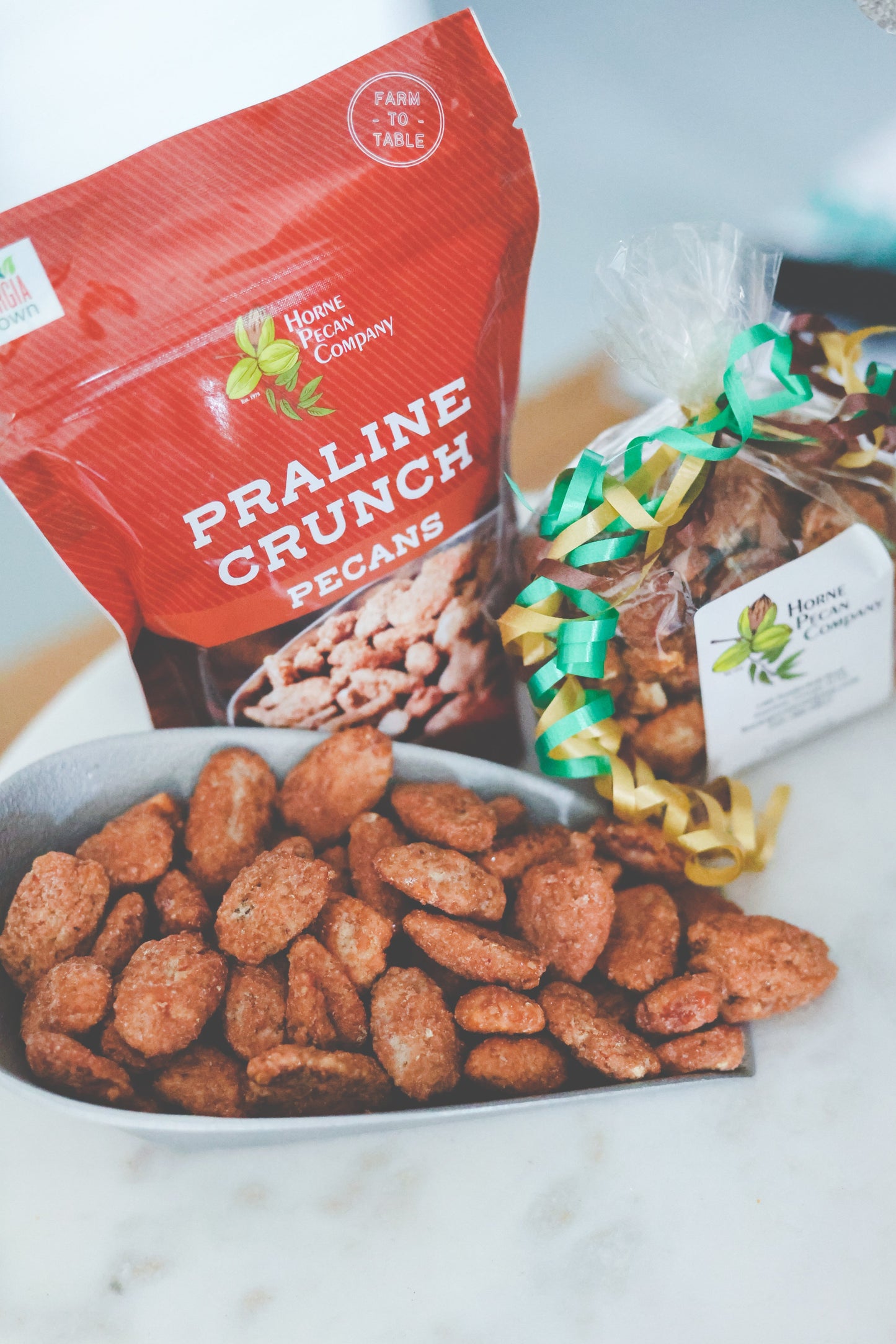 Horne Pecan Company praline-coated pecans in a clear bag, showcasing shiny caramelized candy coating and pecan pieces inside.