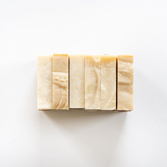 Six unscented MamaSuds No. 12 Bar Soaps, in shades of cream and beige, are arranged vertically on a white background. These rectangular bars are made with certified organic, vegan, and cruelty-free ingredients.