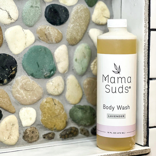 A bottle of MamaSuds Body Wash Soap rests on a bathroom shelf, framed by colorful smooth stone tiles.