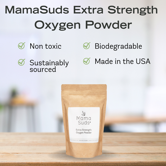 A brown pouch labeled MamaSuds Extra Strength Oxygen Powder, a powerful bleach alternative and stain remover, sits on a table. The text highlights: Non-toxic, sustainably sourced, biodegradable, and made in the USA. The background is softly blurred.