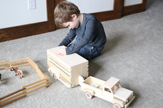 Amish-made wooden pickup truck and horse trailer toy set, unfinished, with detailed farm vehicle and horse figures on a wooden surface.