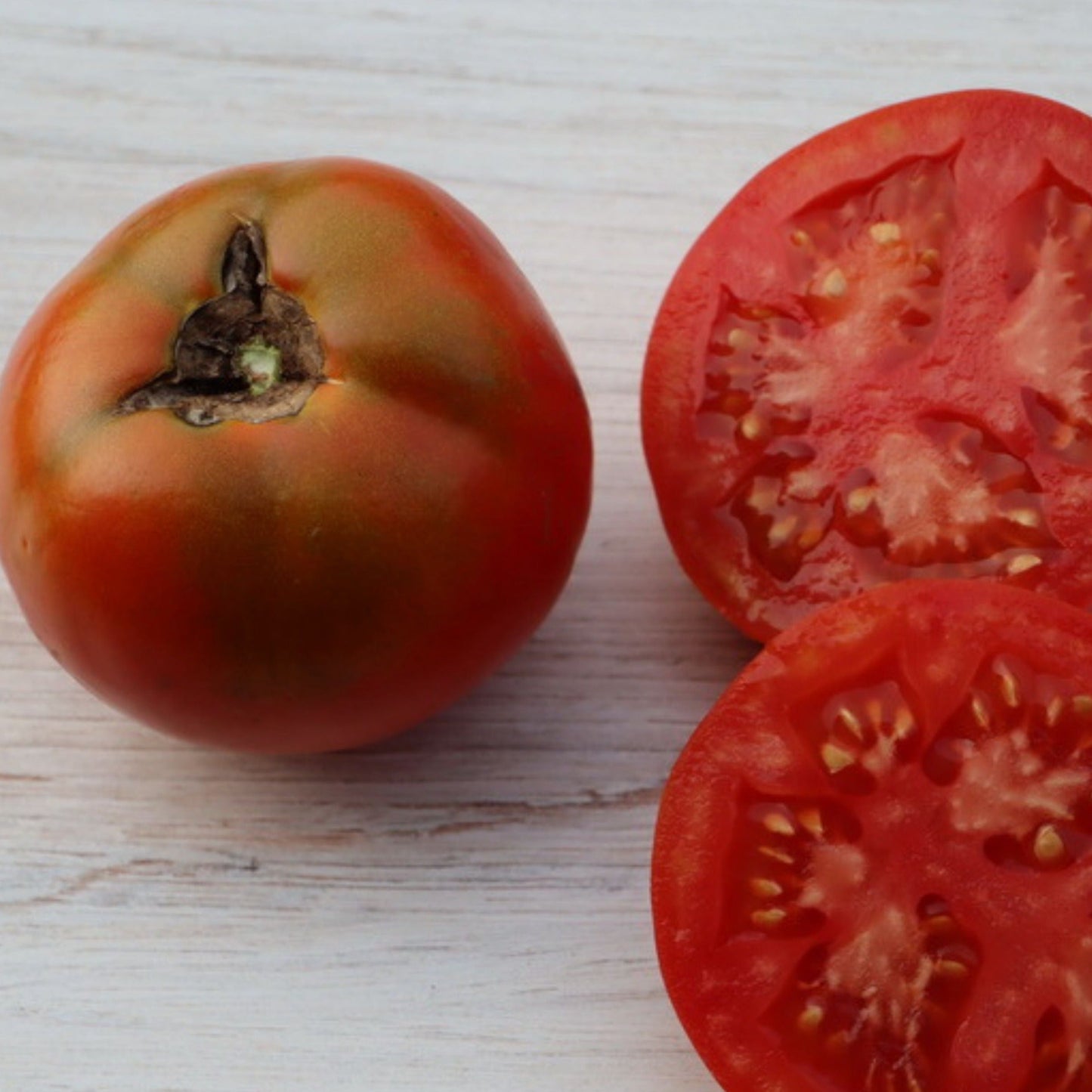 Fresh Druzba tomato from MIgardener showing ripe, red, round fruit with green stem on a plant.