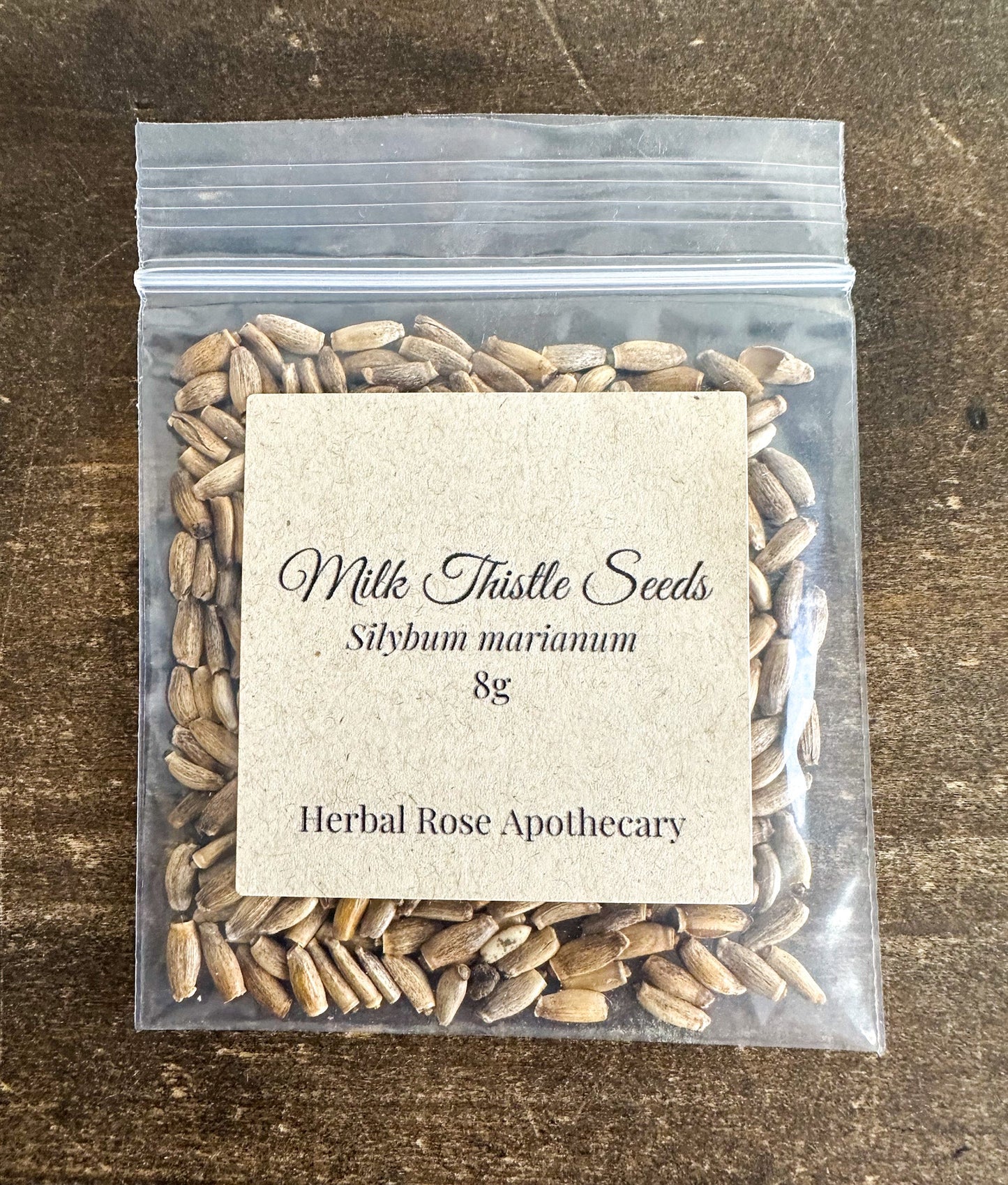 Dried milk thistle seeds from HerbalRoseApothecary, 8g, showing small, dark herbal seeds on a white background.