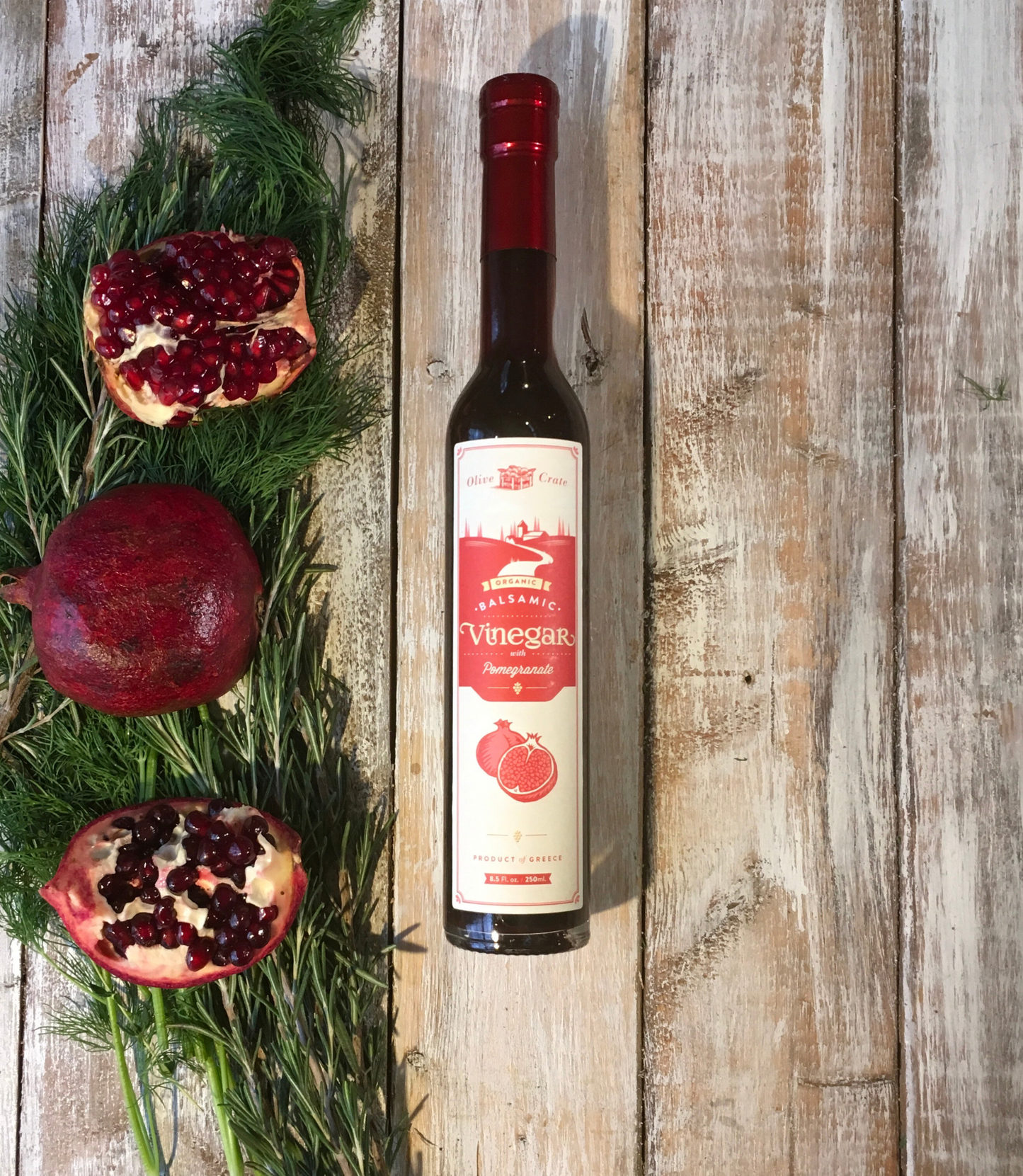 Glass bottle of Olive Crate 100% organic balsamic vinegar with pomegranate, featuring dark balsamic and pomegranate seeds inside.