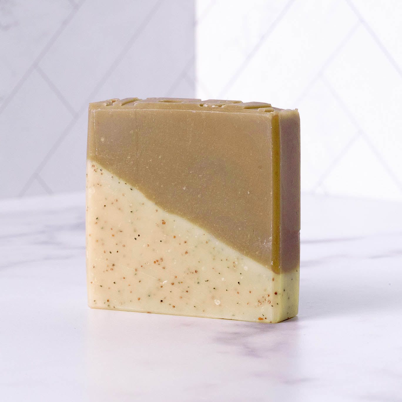 Rustic Strength Bar Soap | Sandalwood Patchouli: A rectangular cold process bar with a light beige, speckled bottom half and solid brown top half, displayed on white marble. Crafted with hydrating natural ingredients.