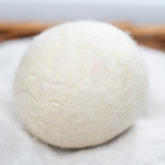 A close-up of a Rustic Strength Jumbo Wool Dryer Ball (3 pack), made from eco-friendly wool, resting on a light-colored fabric surface.