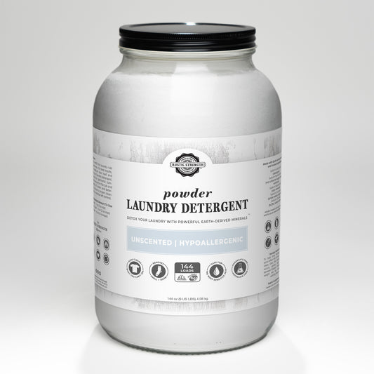A large glass jar of Rustic Strength Powder Laundry Detergent features a white label with product details and icons for earth-derived minerals. This unscented, hypoallergenic powder is gentle on sensitive skin.