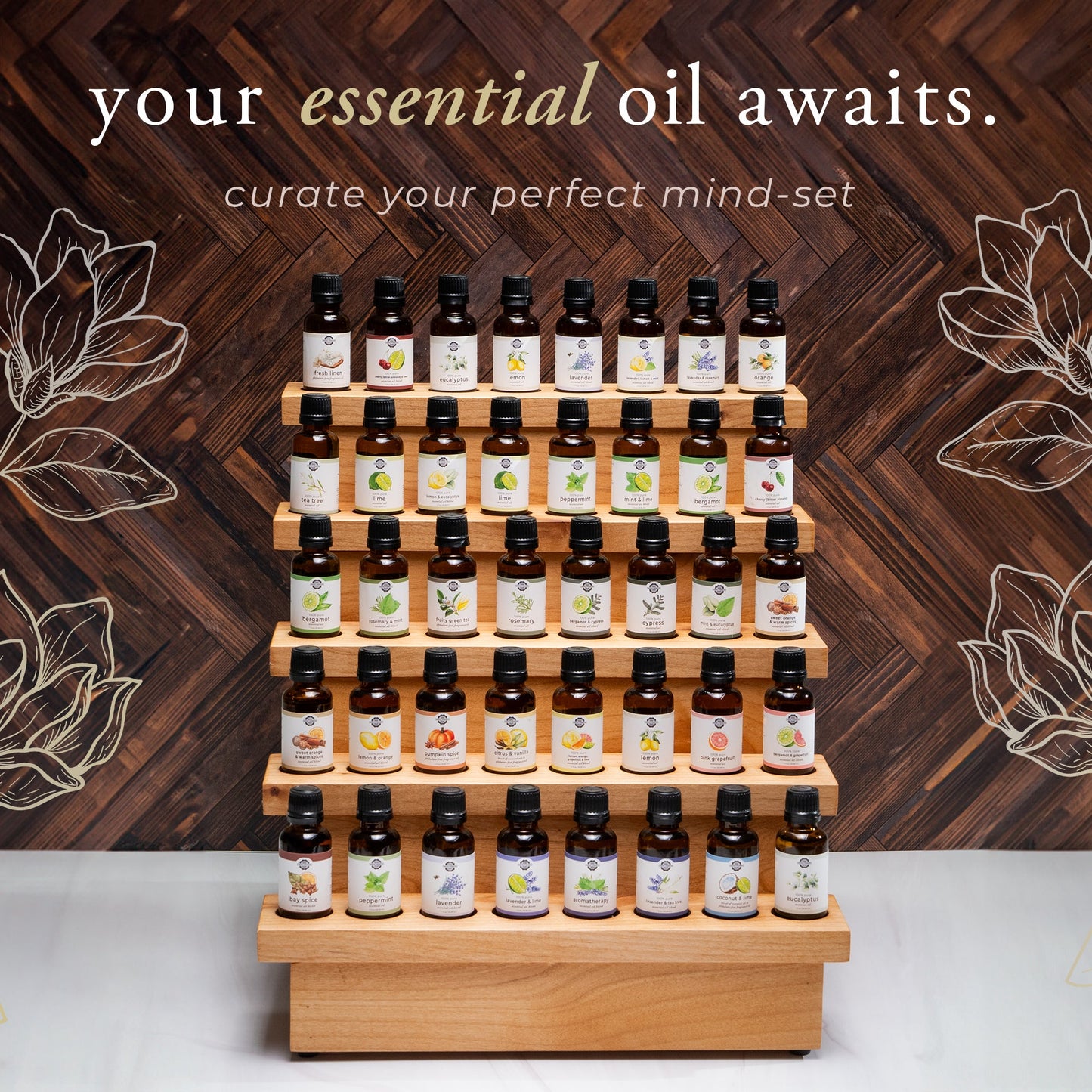 A wooden display stand holds five rows of Rustic Strength Bergamot & Grapefruit Essential Oil Blend bottles, each labeled uniquely. Floral line art and the text your aromatherapy awaits invite you to curate your perfect mind-set.