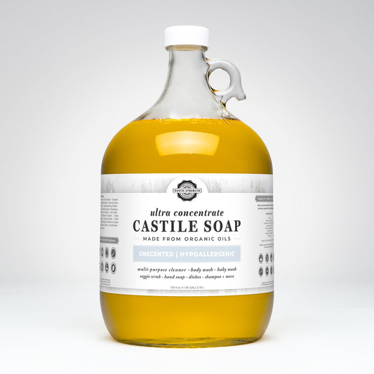 A large, clear glass jug with a white cap and handle contains Rustic Strength Castile Soap - Ultra Concentrate | Unscented, made from organic oils. This hypoallergenic soap is perfect as a multi-purpose cleaner.
