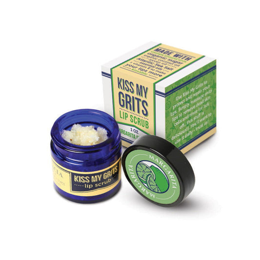 A small blue jar of Salacia Salts Kiss My Grits Lip Scrub, a grainy pale exfoliating treatment, sits open beside its matching box and black lid with a green leaf logo.
