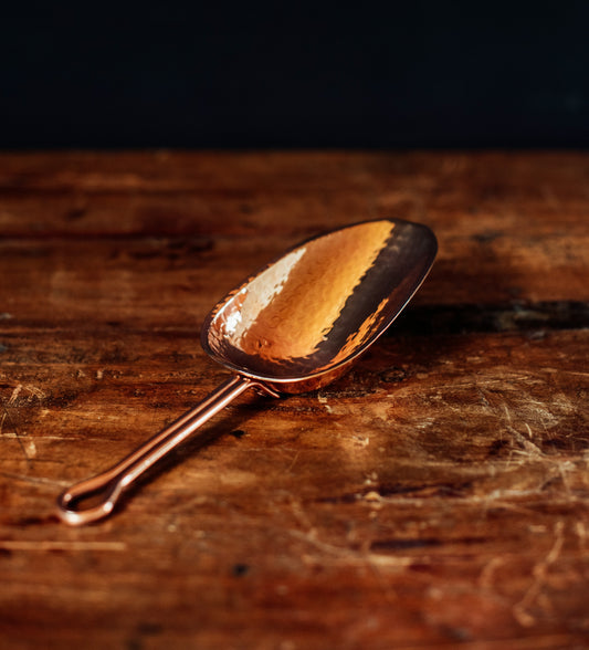 Sertodo copper scoop lying down, barware and bar tool used for serving and measuring ingredients in cocktail preparation.
