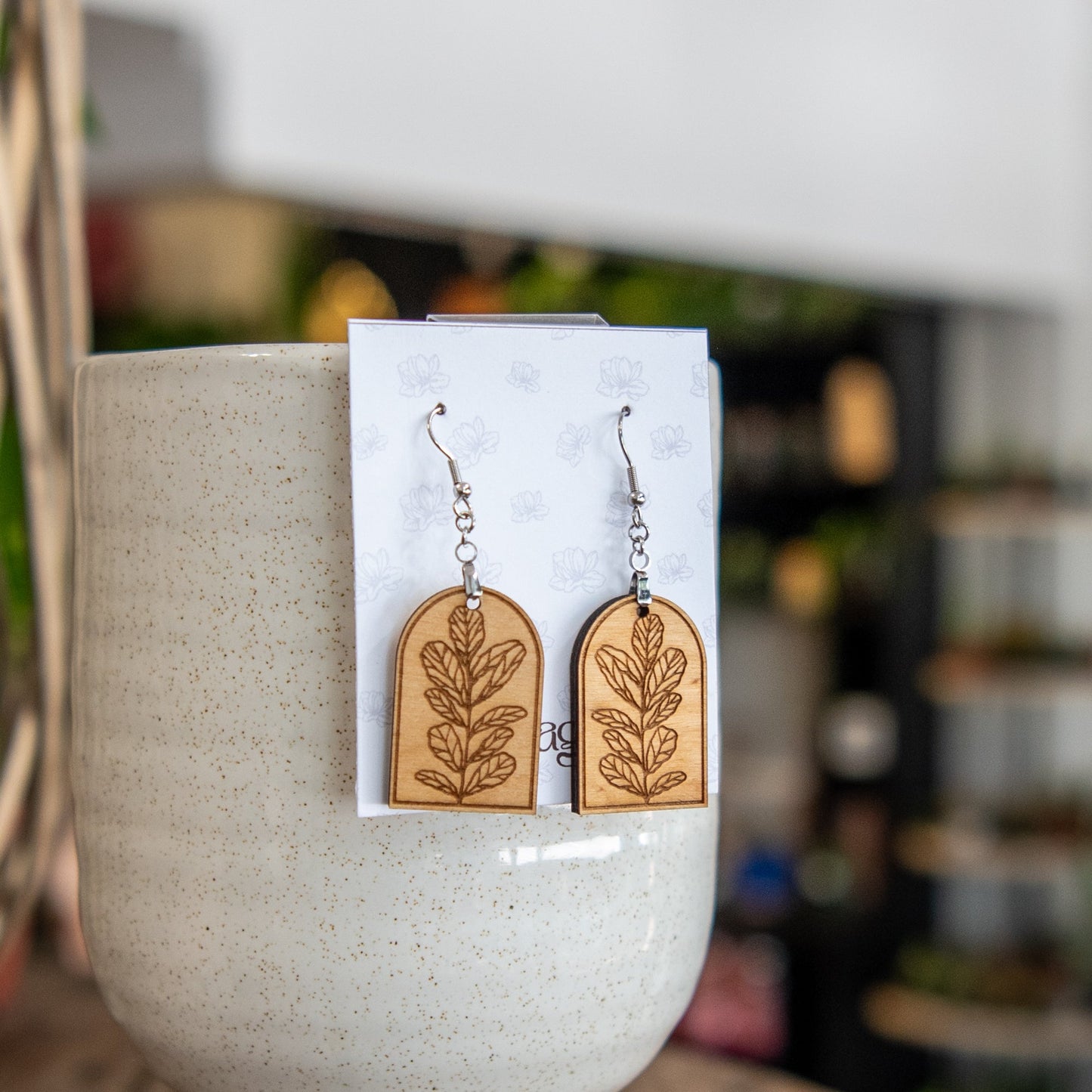 Still Magnolia Fiddle Leaf Fig Arched Earrings, gold-tone earrings with leaf-inspired design, hanging from ear.