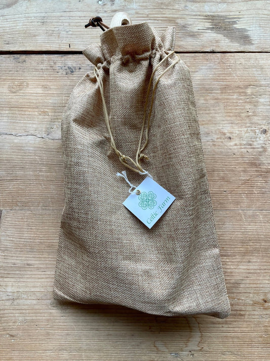 A rustic drawstring burlap bag with a The Celtic Farm tag sits on wood, ideal for gifting the Seed & Bulb Planters Tool Set—three essential planting tools perfect for gardeners and garden tool collections.