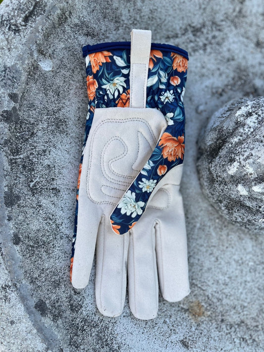 The Celtic Farm Womens Floral Gardening and Project Gloves The Olivia, featuring beige palms and a blue floral pattern, rest on a rough, weathered stone surface.