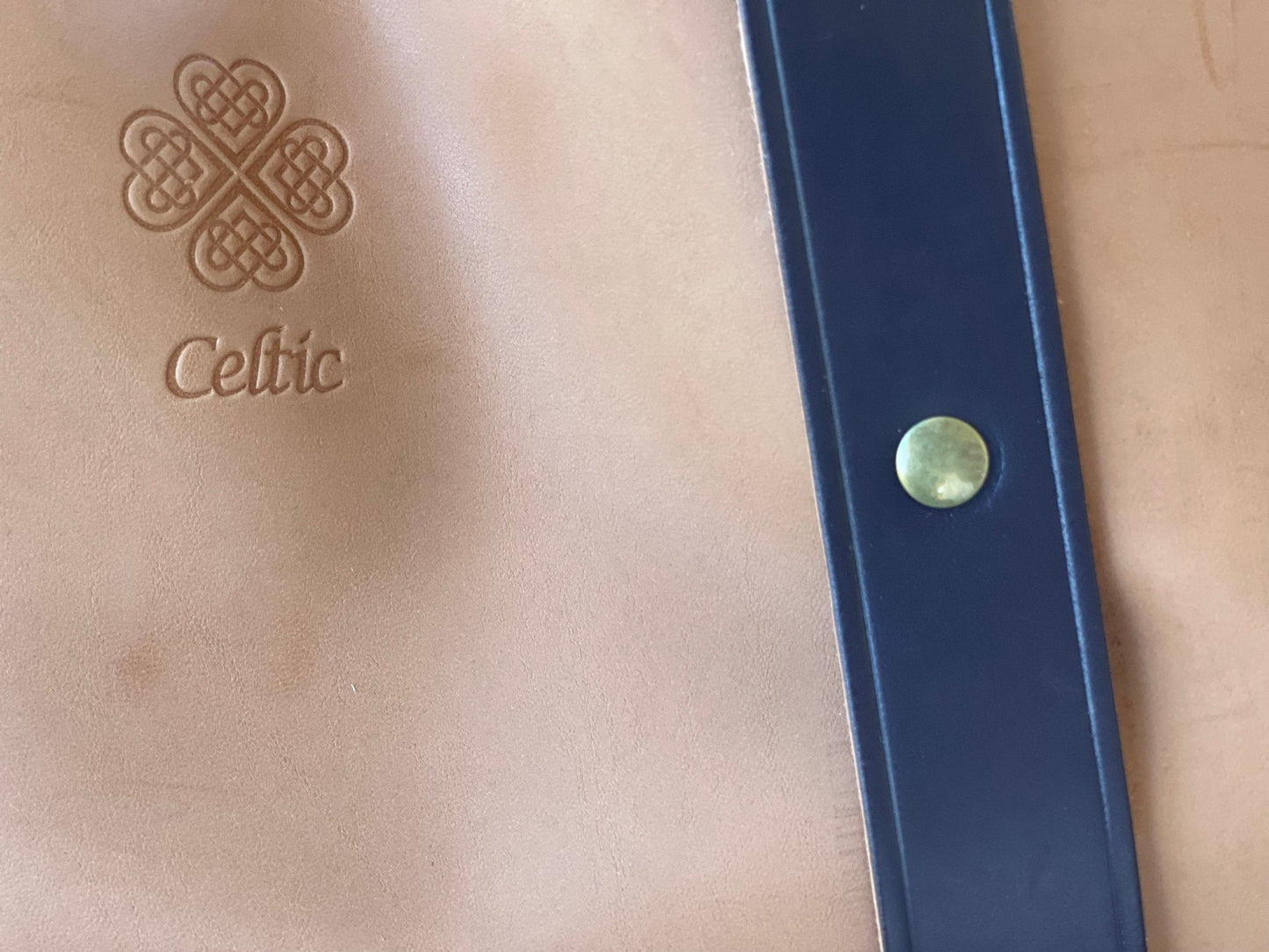 The Celtic Farm Leather Gardeners Tool Bag features tan leather, a Celtic knot design, Celtic embossing, and a dark blue strap with brass rivet—a unique carryall and ideal gardening gift.