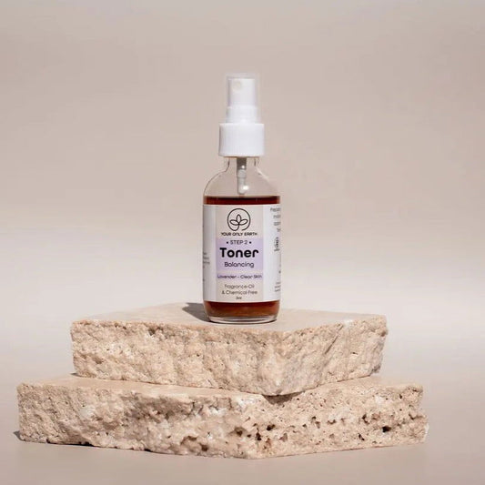 Two tubes of Your Only Earth Toner stand upright on rough stone slabs. Digital glitches distort the image, obscuring the labels and details against a plain, neutral background.