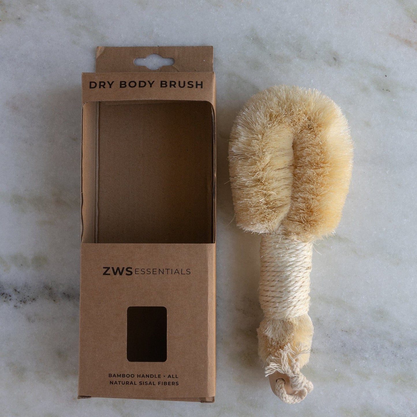 A ZeroWasteStore.com Dry Body Brush with a bamboo handle and sisal bristles sits beside its cardboard box on a marble surface. The packaging indicates it supports lymphatic drainage for radiant skin.