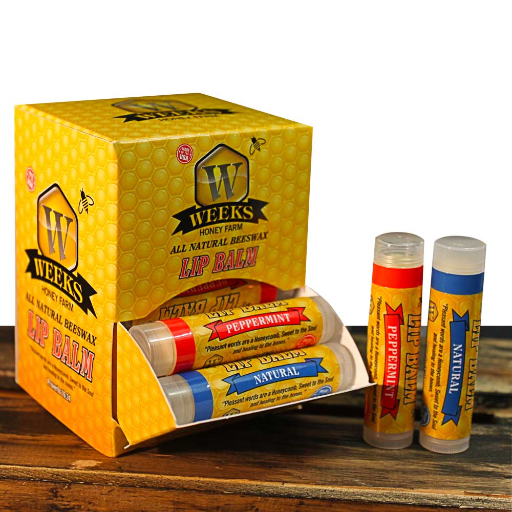 A yellow honeycomb-patterned Weeks Honey Farm box labeled Weeks All Natural Beeswax Lip Balms holds lip balm tubes in peppermint and natural flavors, with two singles displayed outside on a wooden surface. Available in singles, twin packs, or by the case.