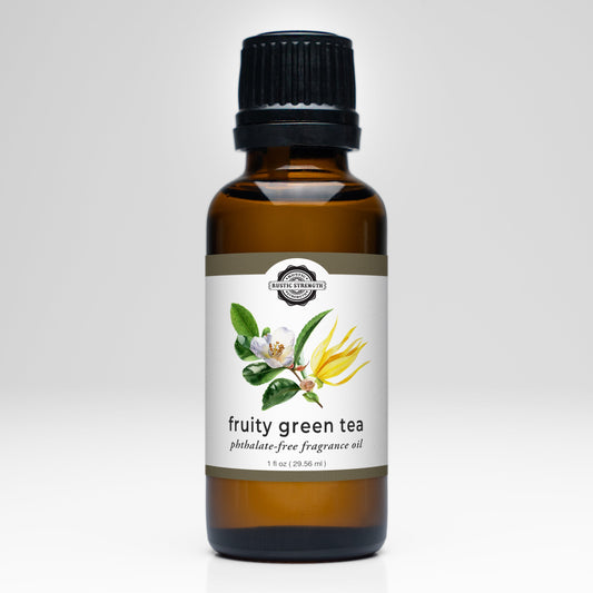 A brown glass bottle with a black cap labeled Fruity Green Tea Phthalate-Free Fragrance Oil by Rustic Strength, featuring an illustration of tea leaves, white flowers, and yellow blossoms on the front.