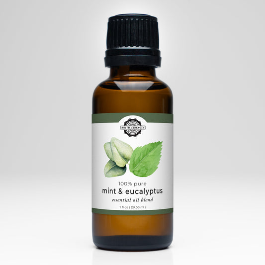 Rustic Strength Mint & Eucalyptus Essential Oil Blend comes in a brown glass bottle with a black cap, featuring illustrated mint leaves and eucalyptus on the label—ideal for aromatherapy or blending with other oils. Shown against a white background.