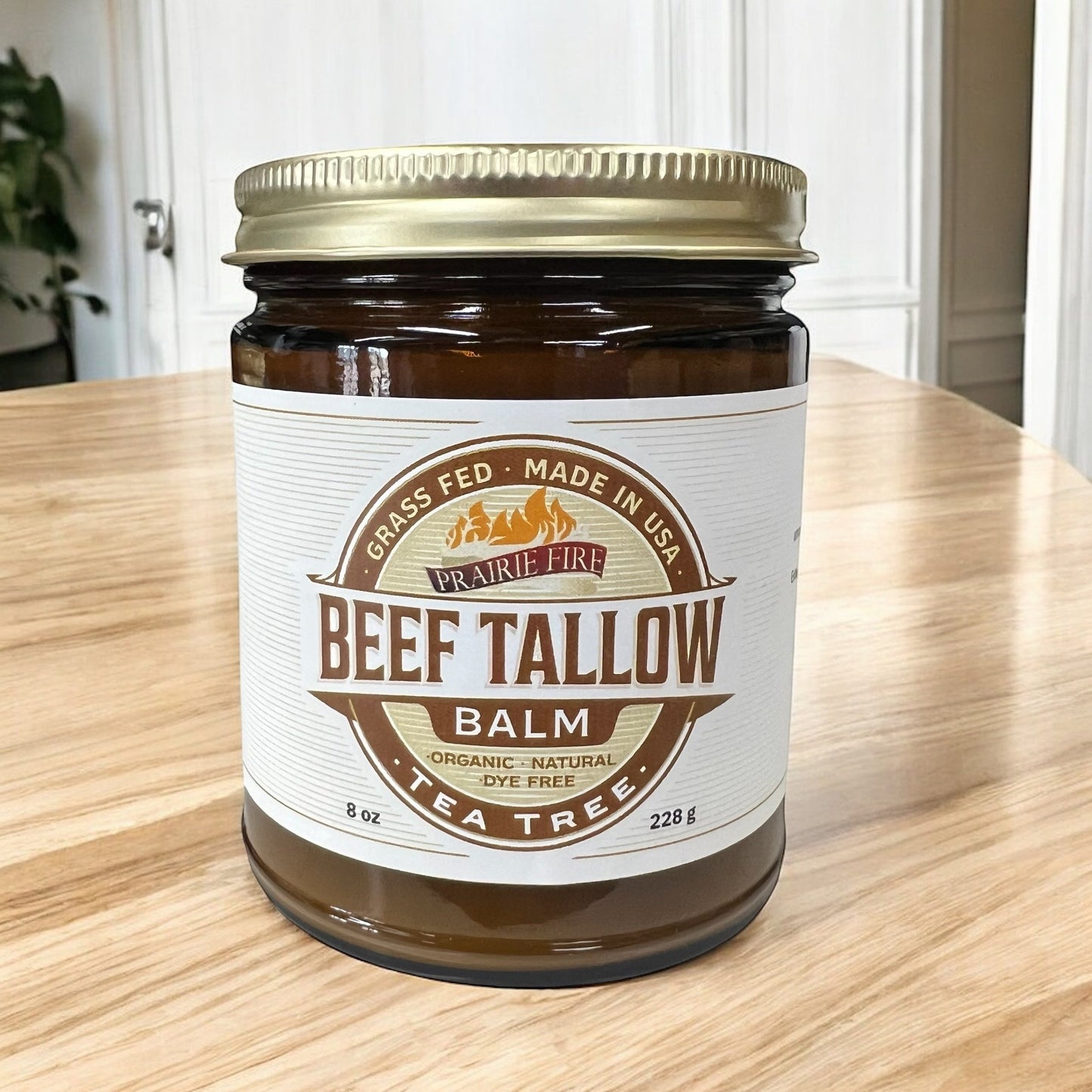 A jar of Prairie Fire Tallow, Candles, and Lavender Beef Tallow Balm (8 oz) rests on wood. This organic, grass-fed, USA-made moisturizer with tea tree oil is dye-free and highlights its pure ingredients on the label.