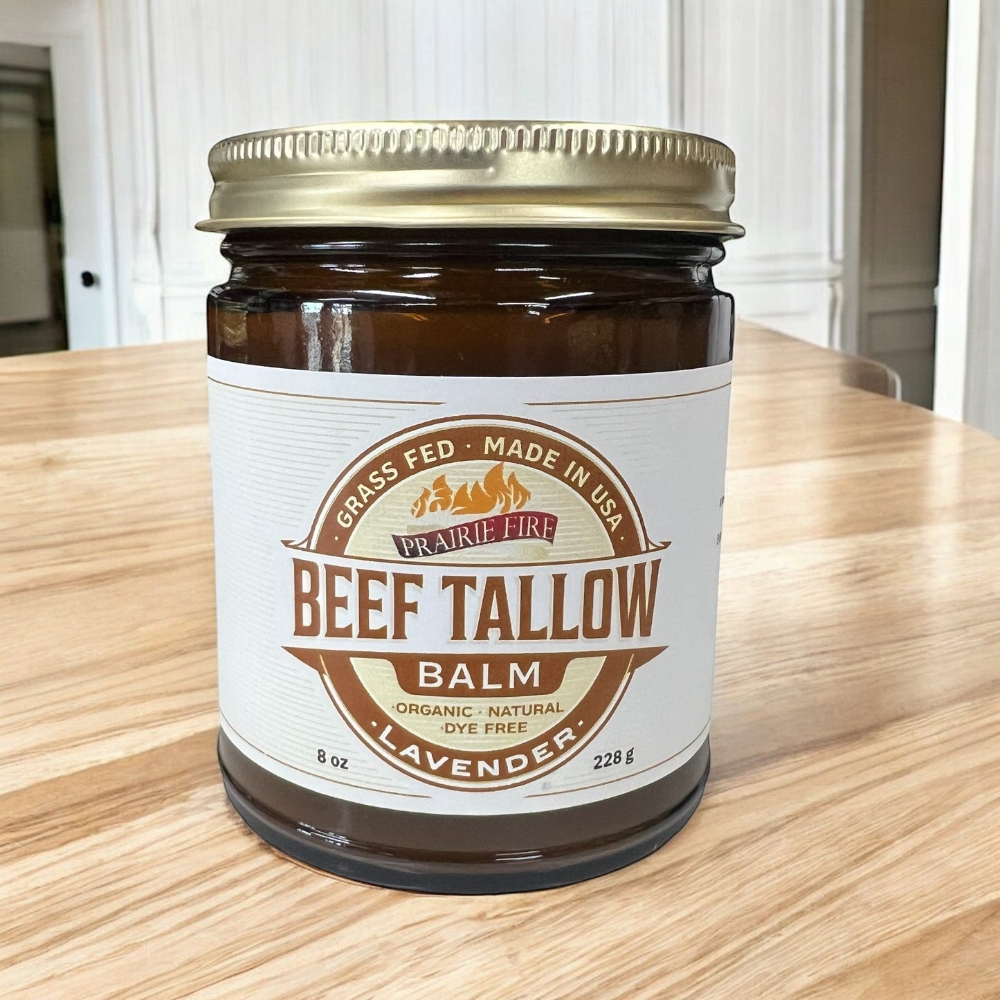 A glass jar of Prairie Fire Tallow, Candles, and Lavender’s Beef Tallow Balm (8 oz), an organic, grass-fed moisturizer made in the USA with a lavender scent and dye-free formula, sits on a wooden table.