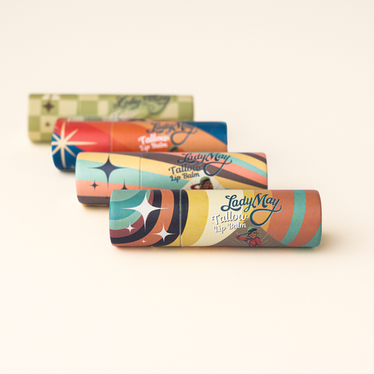 Four colorful tubes with retro designs are arranged diagonally on a white surface. Closest is Lady May Tallow Lip Balm by Lady May Tallow, an all natural beef tallow lip balm that provides deep hydration and natural care for your lips.